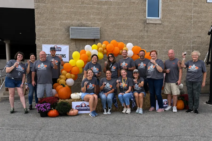 Adult Oktoberfest volunteers in matching shirts raising a toast by the balloon arch