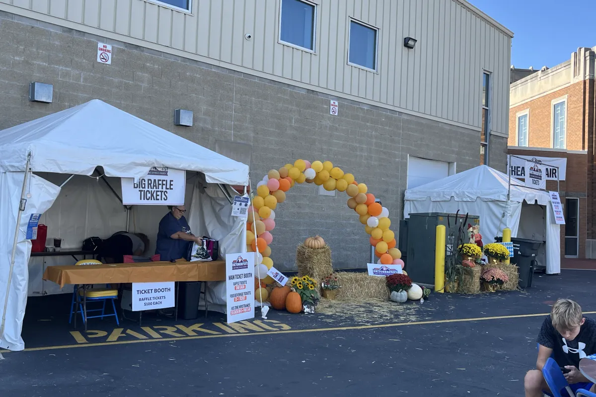 The Big Ticket Raffle booth with signage, balloon arch, pumpkins, and hay bales at Holy Name Oktoberfest