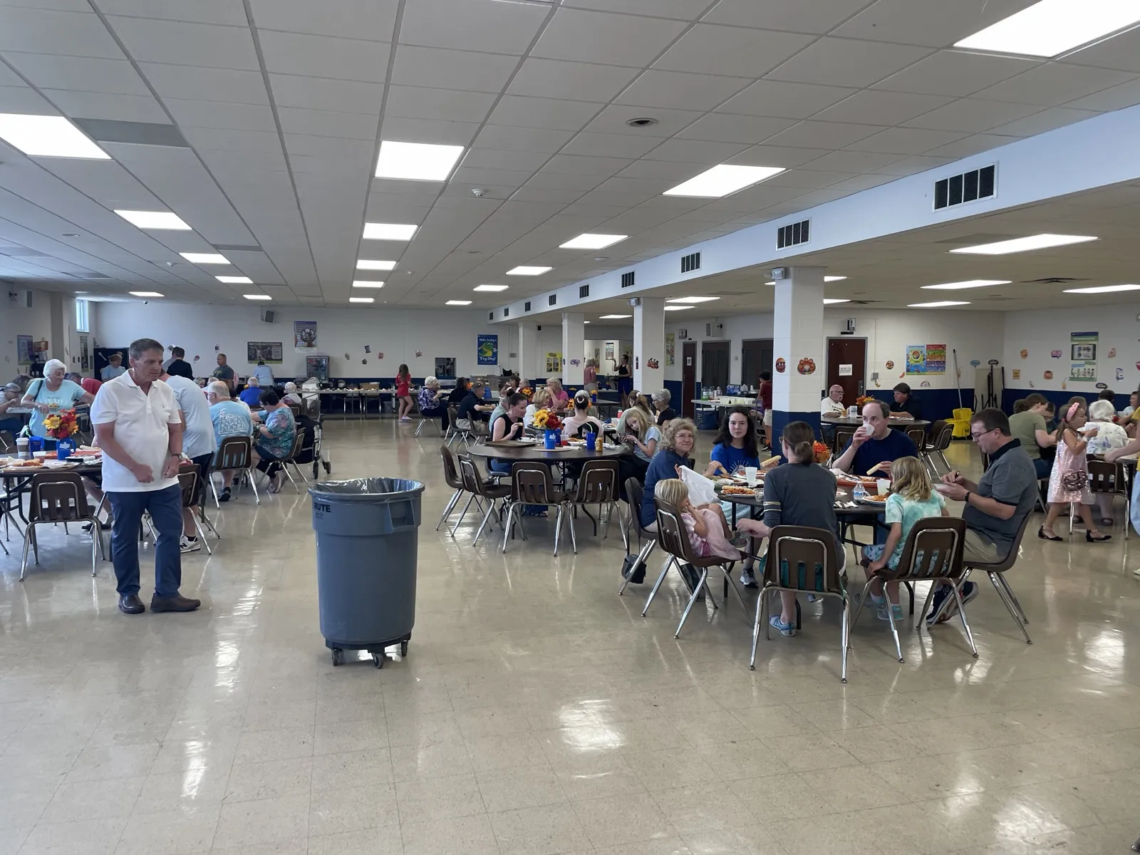 Families seated at round tables eating spaghetti across a full school cafeteria